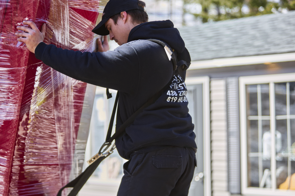 Un déménageur en train de porter un meuble lourd, en extérieur, lors d'un déménagement.