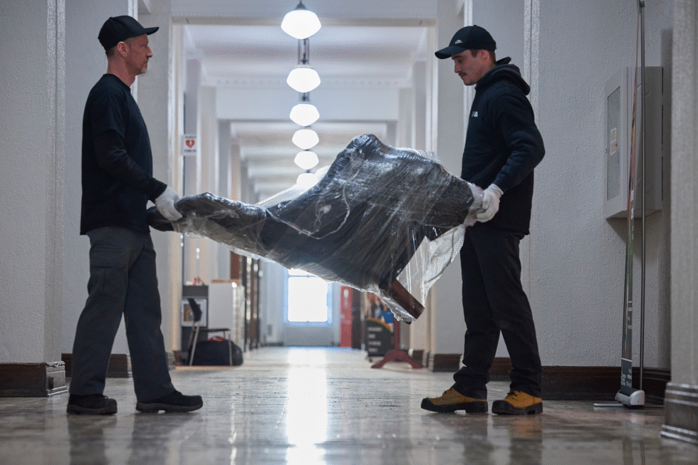 Une vue latérale de nos deux déménageurs qui transportent un fauteuil emballé lors d'un déménagement dans un musée.